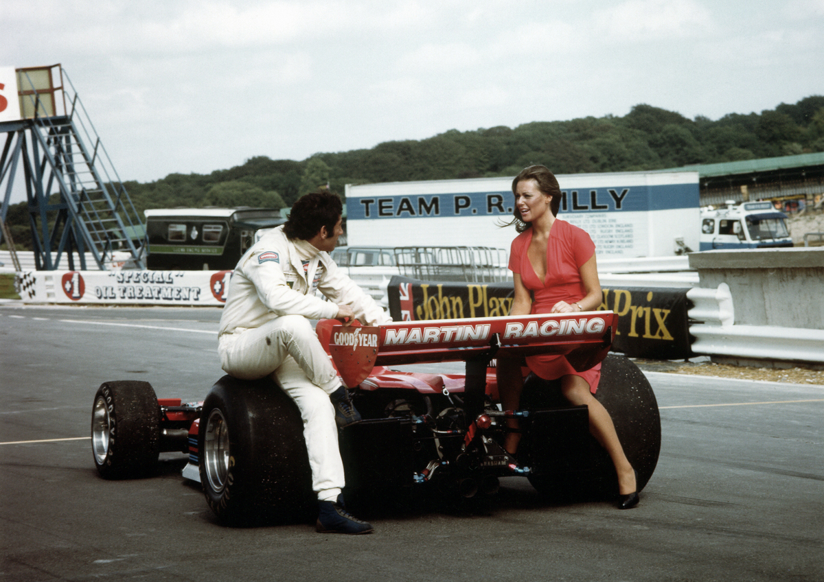 Carlos Pace unterhält sich mit einer Freundin, auf den Hinterreifen seines Brabham-Alfa Romeo BT45 von 1976 sitzend