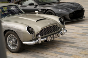 Bild Aston Martin DB5 (2020) - Filmauto aus "Keine Zeit zu sterben" mit Gatling-Guns und Kampfspuren, dahinter ein moderner DBS