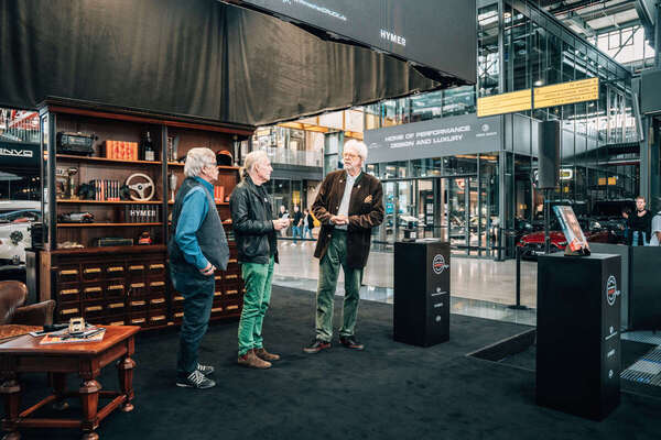 Image: On stage with a bookshelf and a filing cabinet—the set design evokes a library rather than a showroom