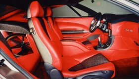 Bertone Bella (1999) – Innenraum in kräftigem Rot. Der linke Rücksitz ist zum Laderaum umgebaut, darunter das Vorderrad von "La Bestia". Instrumente und Mittelkonsole sind (leicht individualisiert) vom Alfa Romeo 166 übernommen Bertone Bella (1999) – Innenraum in kräftigem Rot. Der linke Rücksitz ist zum Laderaum umgebaut, darunter das Vorderrad von "La Bestia". Instrumente und Mittelkonsole sind (leicht individualisiert) vom Alfa Romeo 166 übernommen