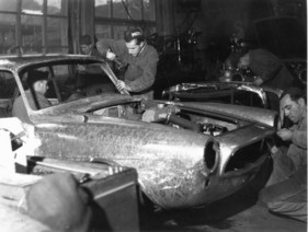 Bild Beutler (1959) - Produktion - während ein Arbeiter das Ziergitter vorne einpasst, verkleidet ein anderer die A-Säule, im Hintergrund werden die Stosstangen fertiggestellt