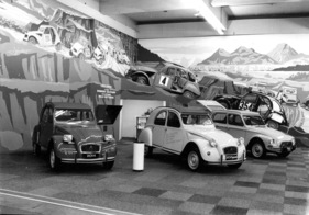 Citroën 2 CV (1976) - attraktiver Standaufbau mit Rallye-Autos im Hintergrund - Genfer Autosalon 1976