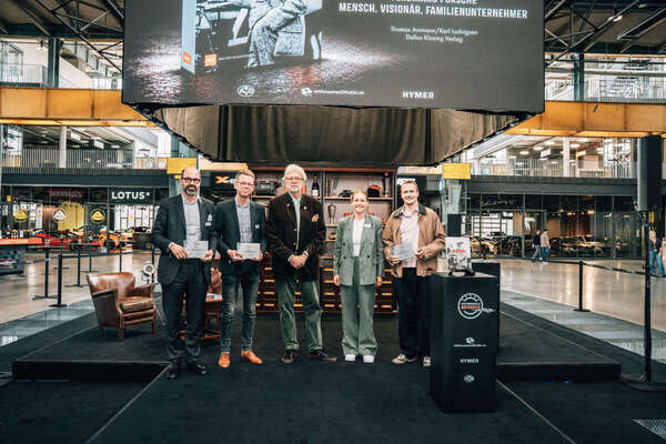 The award recipients with their certificates for the Honorary Biography Award—behind them, the cover of the Porsche biography published by Delius Klasing Verlag
