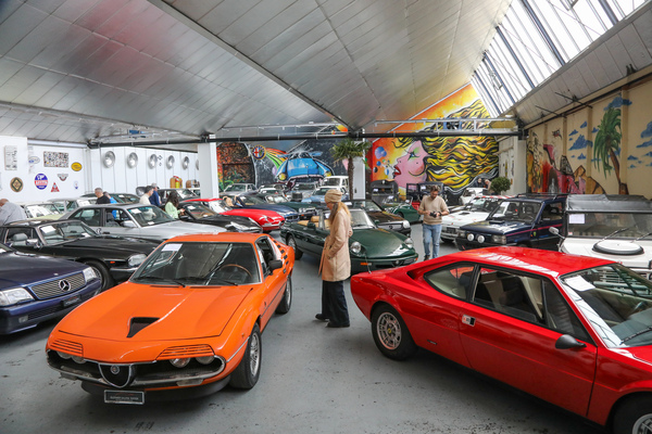 Ein oranger Alfa Romeo Montreal neben einem Dino 208 GT4 im Besichtigungsraum - Versteigerung der Oldtimer Galerie Toffen am 22. März 2025