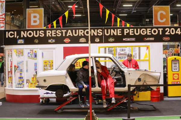 Hier wird ein Peugeot 204 restauriert, allerdings scheint sich der Nachwuchs lieber mit dem Handy zu befassen – Rétromobile Paris 2025