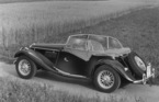 MG Midget Series TF (1954) - im Jahre 1954 nachbearbeitetes Foto, das den Wagen von schräg hinten mit montierten Seitenscheiben aber ohne Dach zeigt
