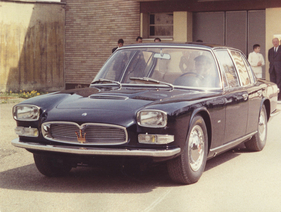 Maserati Quattroporte I (1963) - der zweite Frua-Prototyp - (Chassisnr. 107.004) mit Maserati-Mitarbeitern vor dem Bürogebäude auf dem Maserati-Werksgelände in Modena. Am Steuer: Testfahrer Guerino Bertocchi, im Hintergrund (in weißer Tenniskleidung mit kurzer Hose) Omer Orsis Sohn (und heutiger Maserati-Historiker) Adolfo Orsi Jr.