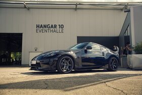Nissan 370Z (2012) - Frontschürze und Schmiedefelgen verschwinden fast im schwarzen Lack, dahinter die Fassade der Eventhalle Hangar 10 Nissan 370Z (2012) - Frontschürze und Schmiedefelgen verschwinden fast im schwarzen Lack, dahinter die Fassade der Eventhalle Hangar 10