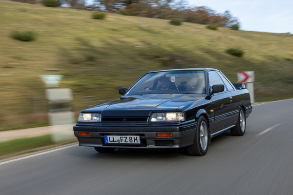 Bild: Nissan Skyline GTS Coupé (R31) (1988) - Vier eckige Scheinwerfer hinter Glas und ein Grill, der kaum Luft durchlässt, aufgenommen bei voller Fahrt
