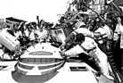 Image: Porsche 956 LH (1982) - Le Mans 1982: Porsche 956 LH at a pit stop, with striped helmet Derek Bell, to his right Jacky Ickx, behind the safety tank refueling race mechanic Gerhard Küchle.