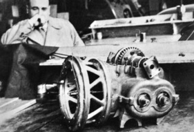 Bild Sacha-Gordine (1953) – Ein nachdenklicher Sacha Gordine studiert den Antrieb: Kupplungsgehäuse, querliegendes Getriebe, darüber Differentialgehäuse und Flansche für die Halbwellen