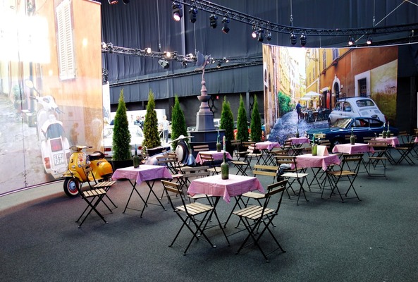 Bild Strassencafé mit Vespa und Fiat 850 Sport Coupé vor lebensgrossen Fotos italienischer Altstadtgassen – Ausstellung "125 Jahre Fiat" in der Autoworld Brüssel