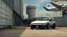 Toyota Sprinter Trueno AE86 (1985) - Geschlossene Klappscheinwerfer, dahinter Frachtcontainer und ausgemusterte Verkehrsflugzeuge Toyota Sprinter Trueno AE86 (1985) - Geschlossene Klappscheinwerfer, dahinter Frachtcontainer und ausgemusterte Verkehrsflugzeuge